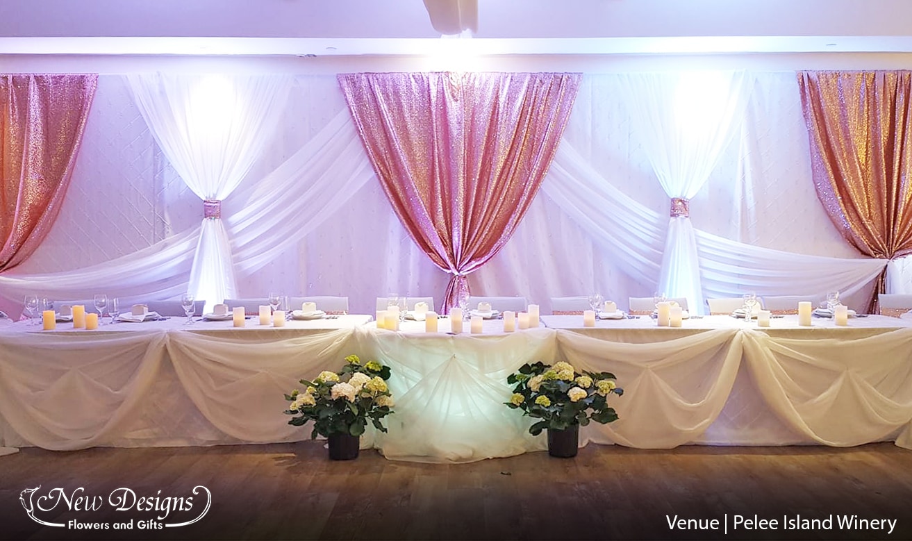 A gorgeous backdrop of crisp white and Sequined Rose gold runs behind a long Head table, with soft draped and cinched chiffon, the middle sweet heart table lit from below.